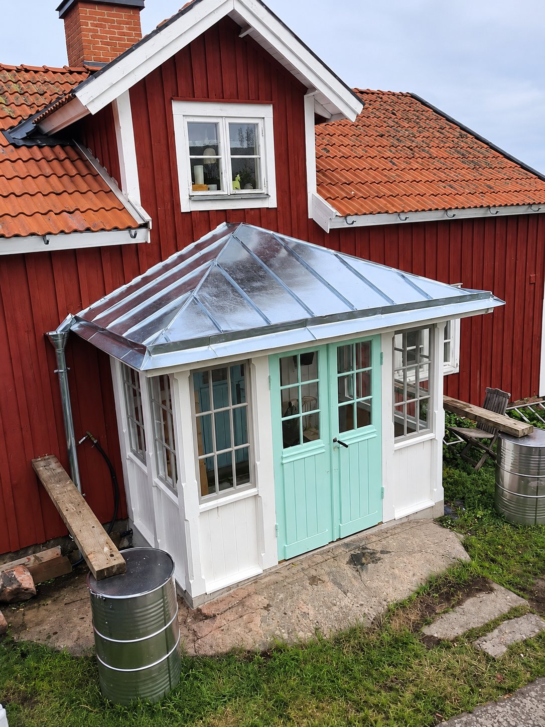 Glasveranda med valmat zinktak framför ett rött trähus