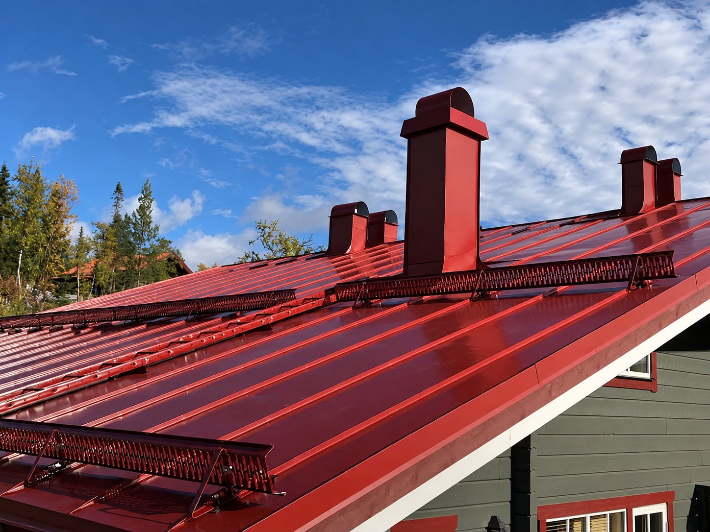 Rött falsat plåttak med snörasskydd, skorsten och ventilationshuvar i samma kulör