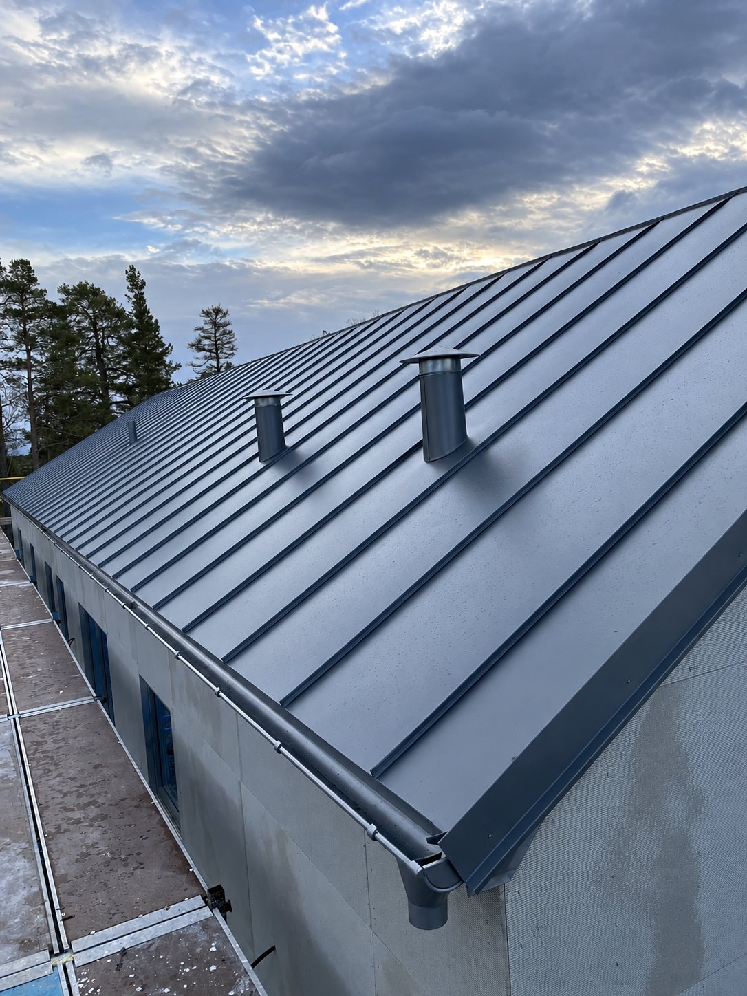 Grått falsat plåttak med ventilationshuvar på en lång byggnad