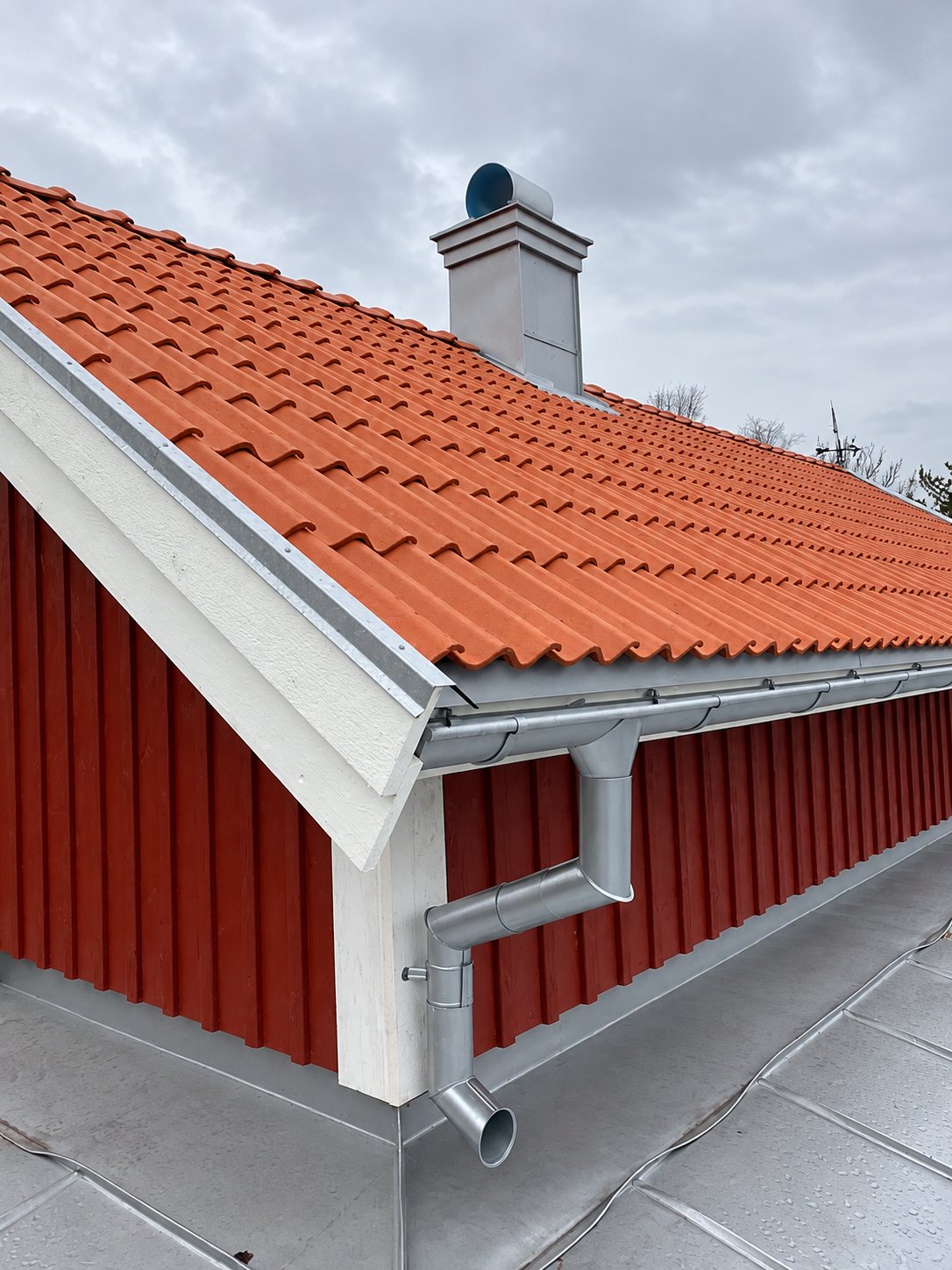 Hängrännor och stuprör i plåt samt plåtinklädd skorsten på rött hus med tegeltak