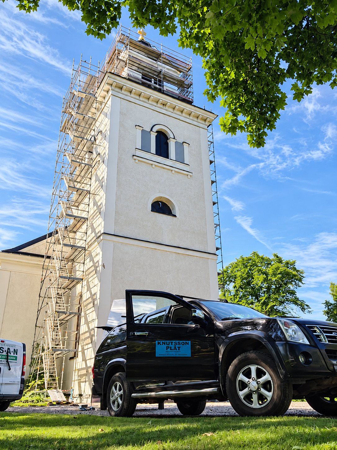 Vitt kyrktorn med byggnadsställning och Knutsson Plåts bil framför
